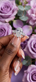 The Duchess pear-cut moissanite ring held in front of purple roses