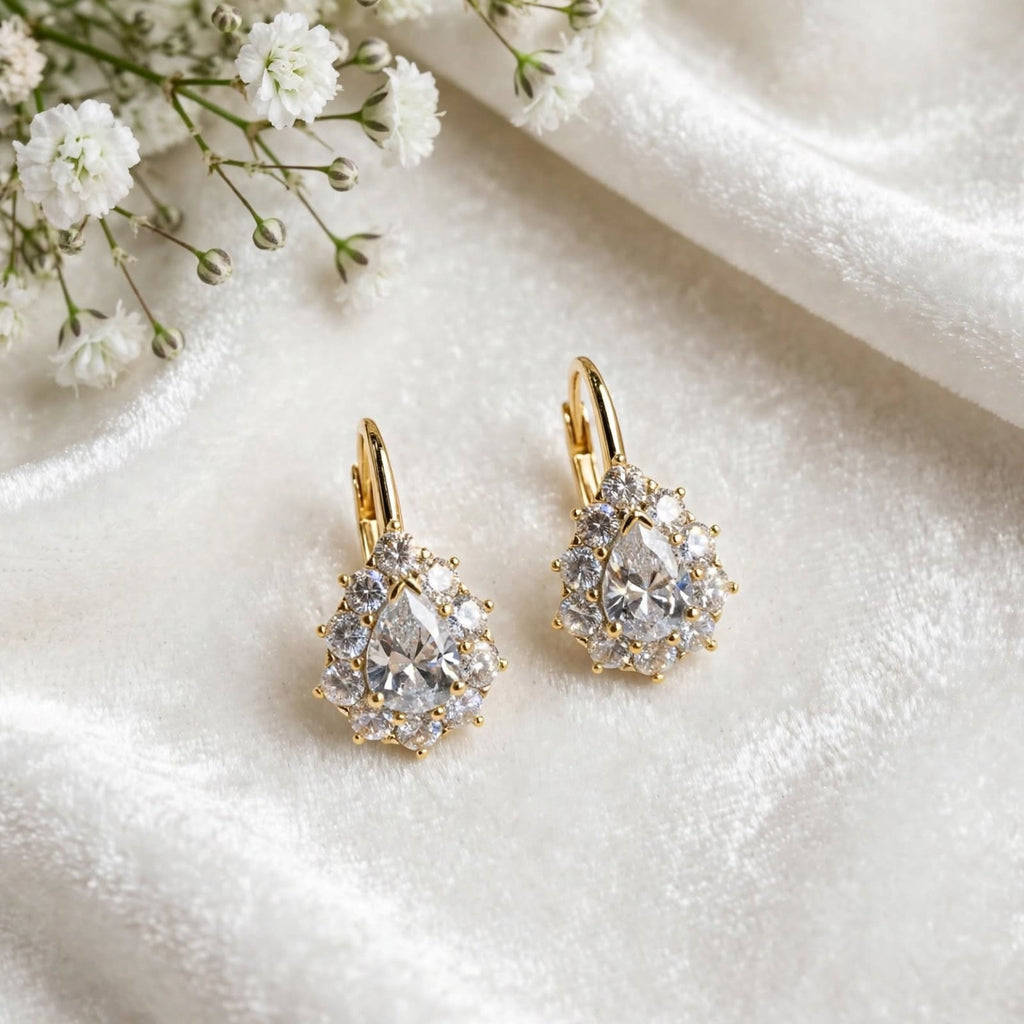 Gold-tone pear-cut halo drop earrings on white satin fabric