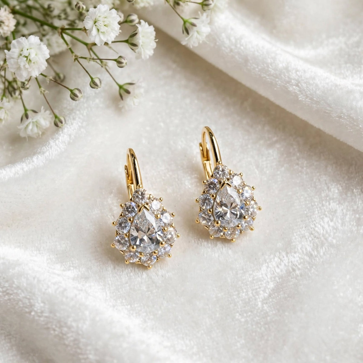Gold-tone pear-cut halo drop earrings on white satin fabric