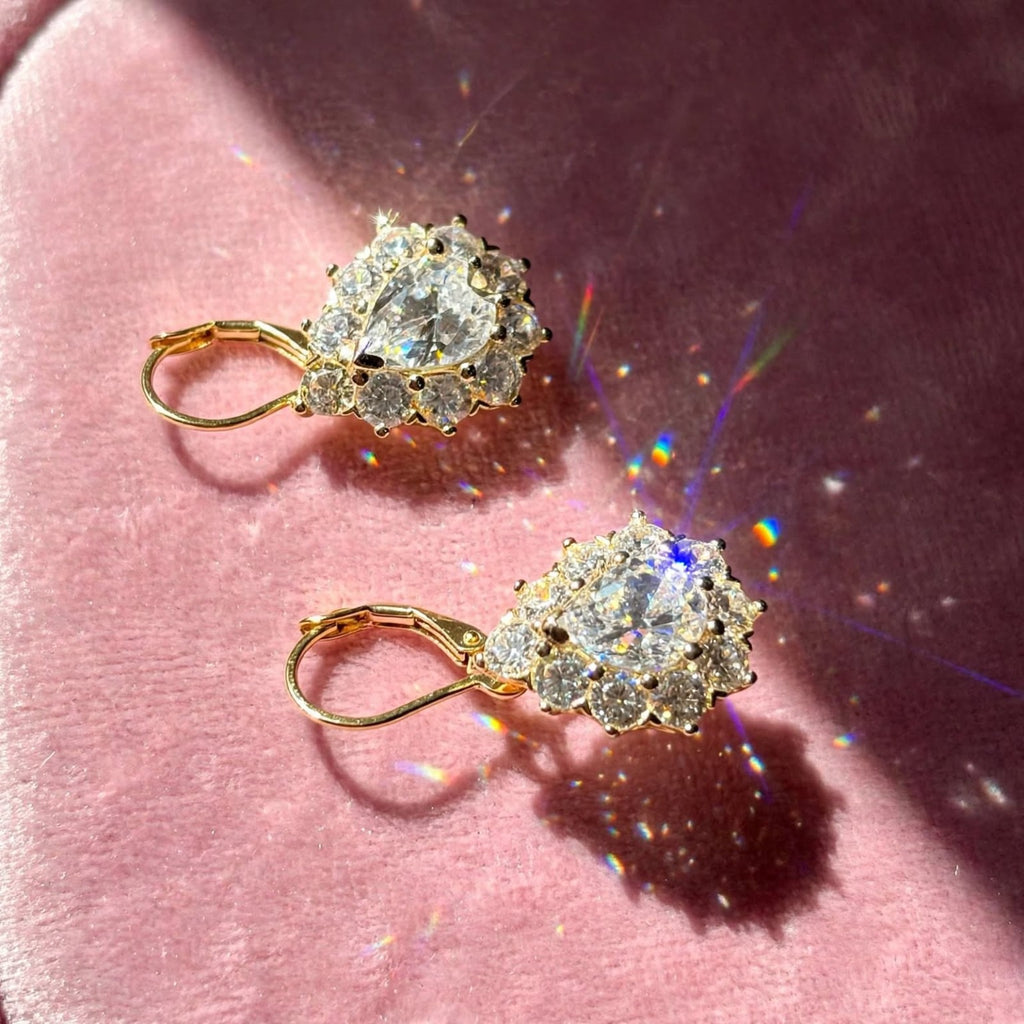 Pair of gold-tone pear-cut moissanite halo earrings on rose velvet