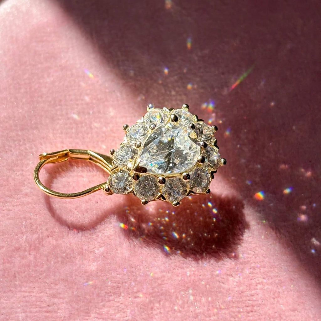 Close-up of one gold-tone pear-cut moissanite halo earring on rose velvet
