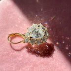 Close-up of one gold-tone pear-cut moissanite halo earring on rose velvet