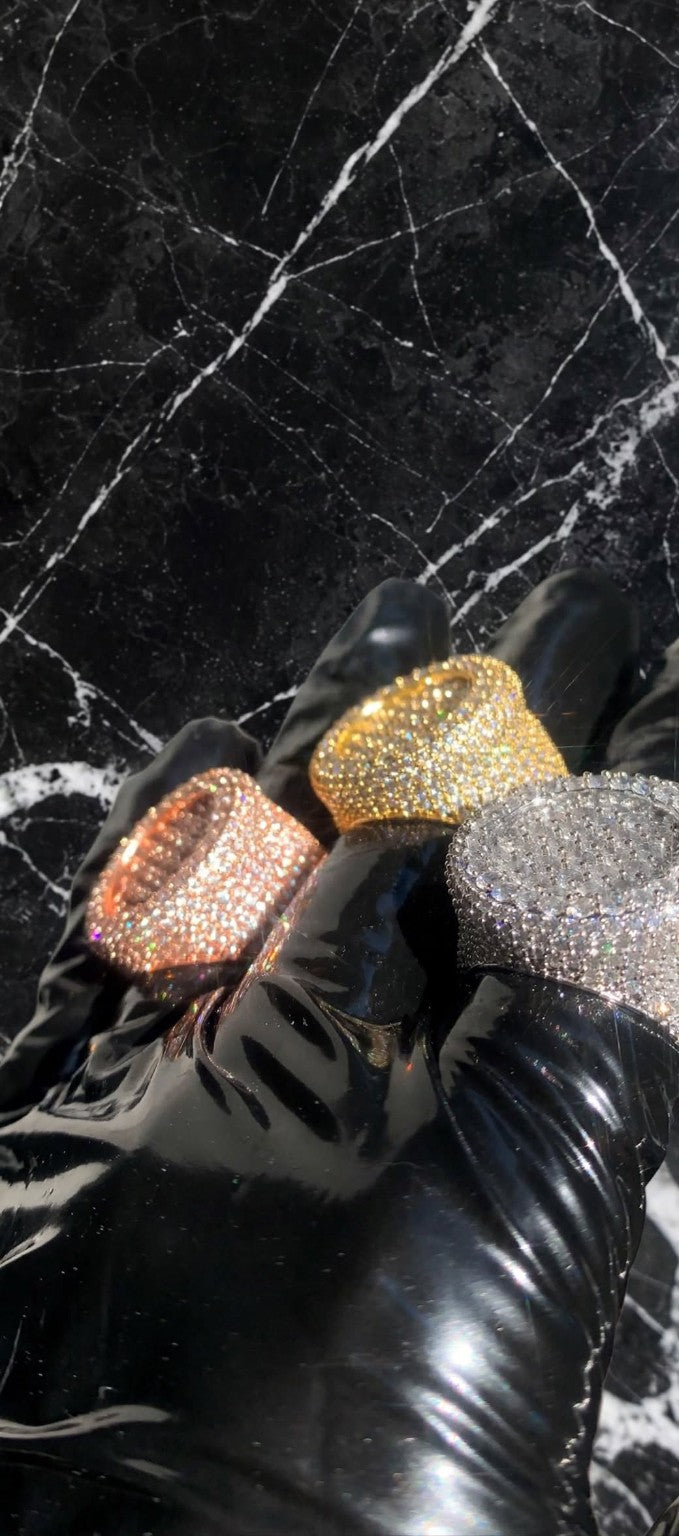 The Introduction fully iced-out statement rings in Gold, Rose Gold, and Silver on black latex gloves